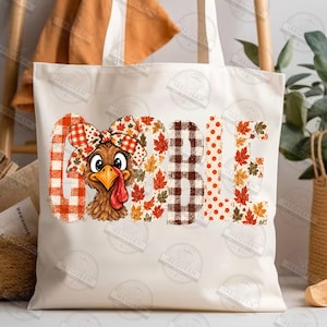 May include: A white canvas tote bag featuring a graphic print of a turkey with a plaid bow on its head. The word GOBBLE is printed in large letters, with the letter O replaced by the turkey, using orange, brown, and red plaid and leaf patterns.