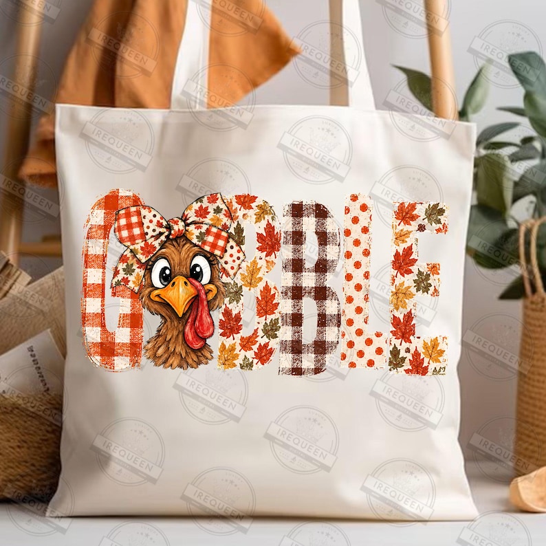 May include: A white canvas tote bag featuring a graphic print of a turkey with a plaid bow on its head. The word GOBBLE is printed in large letters, with the letter O replaced by the turkey, using orange, brown, and red plaid and leaf patterns.