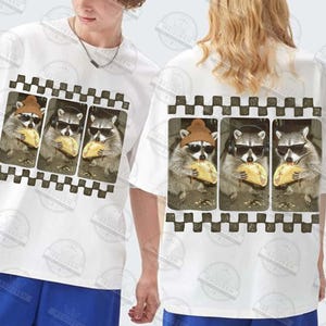 May include: White t-shirt with a graphic of three raccoons wearing sunglasses and eating tacos. The raccoons are in a film strip design with a black and white checkered border. A casual, unisex style.