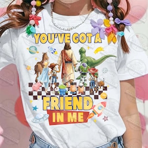 May include: White t-shirt with the text "YOU'VE GOT A FRIEND IN ME" in yellow and red. The shirt features cartoon characters including Jesus, a dinosaur, and characters from Toy Story. A rocket and stars are also included.