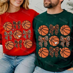 May include: Red and green sweatshirts with basketball and bow designs. The basketballs are orange with black lines. Some bows have a leopard print pattern, and some have a black pattern. Each sweatshirt has a white heart.