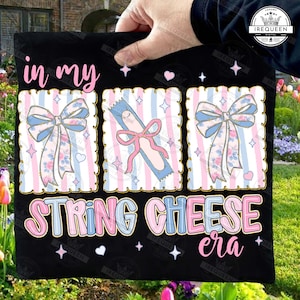May include: Black fabric with the text "in my STRING CHEESE era." The design includes three framed images with bows and string cheese illustrations, set against a pink and blue striped background.
