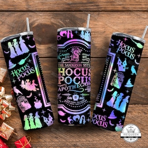 May include: Three black insulated tumblers with a Halloween theme. Each tumbler features the text "Hocus Pocus" and illustrations of witches, bats, and other spooky elements. The design includes a gradient of colors.