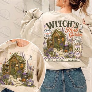 May include: A beige crewneck sweatshirt featuring a graphic print of a garden shed with the text "WITCH'S Herb Garden" and "SAGE POTIONS MOONLIGHT". The illustration includes lavender, a cauldron, and various jars, with additional text labels.