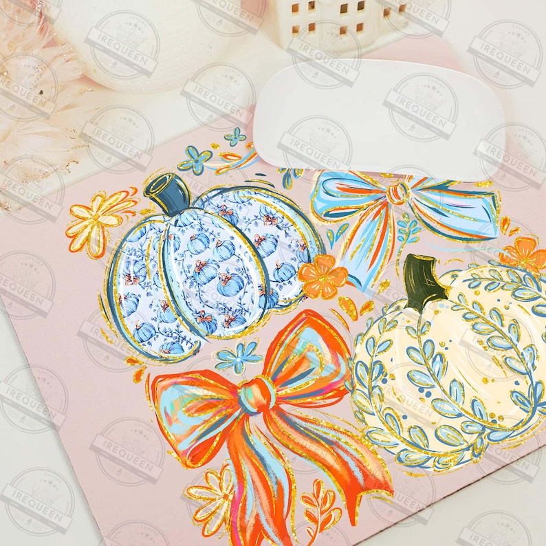 May include: A pink surface with watercolor illustrations of pumpkins and bows. The pumpkins are decorated with blue and white patterns, and the bows are orange and blue. Floral accents complete the fall-themed design.