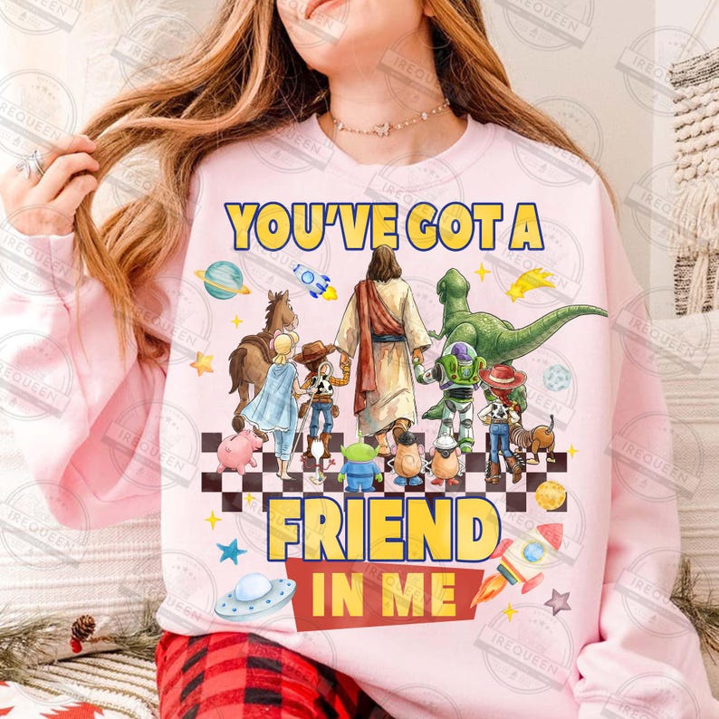 May include: Pink sweatshirt with the text "YOU'VE GOT A FRIEND IN ME" in yellow and red. The design features cartoon characters including Jesus, a dinosaur, and characters from the Toy Story franchise.