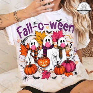 Puede incluir: Una camiseta blanca con un gráfico de tres fantasmas con chicle rosa y bufandas de cuadros. Los fantasmas están rodeados de hojas de otoño naranjas y amarillas, calabazas, una linterna, murciélagos y telarañas. El texto dice Fall-c-ween.