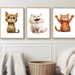 May include: Three framed art prints featuring cartoon cats. The first cat is spotted with large eyes. The second is a fluffy white cat with a wide grin. The third is an orange tabby with its arms raised. The prints are in light brown frames.