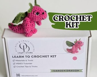 Peut inclure: Un kit de crochet comprenant un petit dragon rose fait main avec des ailes et des cornes vertes. La boîte en carton blanc affiche le texte CROCHET KIT, LEARN TO CROCHET KIT et GARDEN DRAGON, ainsi qu'un logo pour OD Craft Store.