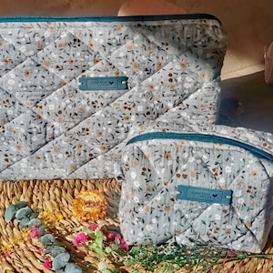 Puede incluir: Dos estuches de cremallera de tela acolchada con un patrón floral. El estuche más grande tiene una cremallera de color turquesa y una etiqueta de cuero marrón que dice "Hand Made with Love". El estuche más pequeño tiene una cremallera de color turquesa y una etiqueta de cuero marrón que dice "Hand Made with Love".