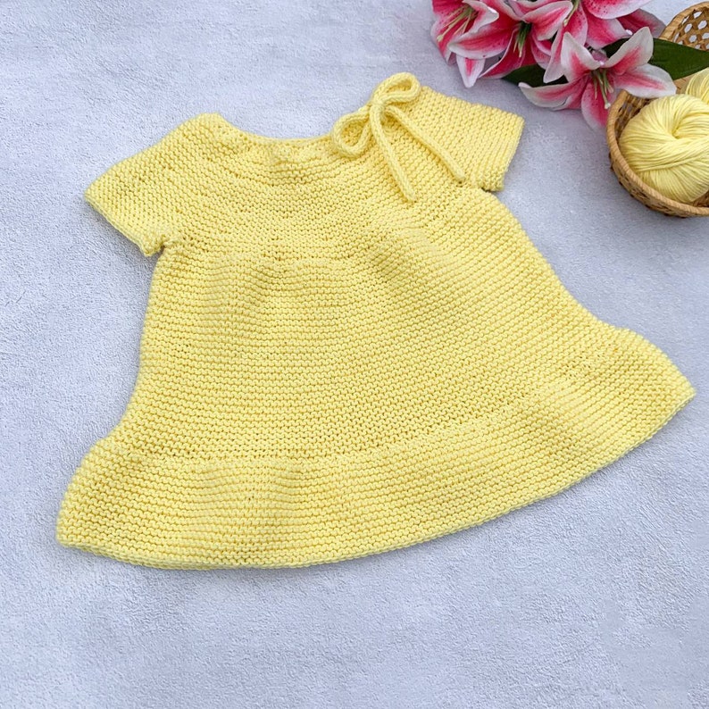 Puede incluir: Un vestido de beb&eacute; de punto amarillo p&aacute;lido con mangas cortas y un lazo en el cuello.