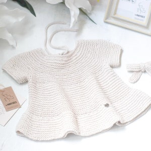 Puede incluir: Un vestido de beb&eacute; de punto de color crema con mangas cortas y un lazo en la espalda. El vestido est&aacute; hecho de una tela suave y ligera y tiene un dise&ntilde;o delicado y femenino. El vestido es perfecto para una ocasi&oacute;n especial o para el uso diario.
