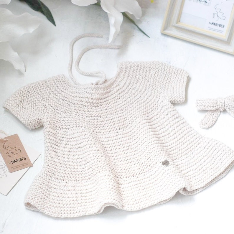 Puede incluir: Un vestido de beb&eacute; de punto de color crema con mangas cortas y un lazo en la espalda. El vestido est&aacute; hecho de una tela suave y ligera y tiene un dise&ntilde;o delicado y femenino. El vestido es perfecto para una ocasi&oacute;n especial o para el uso diario.