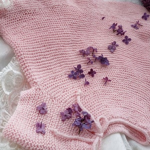 Puede incluir: Una prenda de punto rosa para beb&eacute; con un lazo en el cuello, decorada con flores de lila p&uacute;rpura.