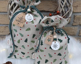 May include: Two small, green and white fabric gift bags with a Christmas tree pattern. The bags have green drawstrings and are decorated with wooden tags that say "Frohe Fest" and a snowflake.