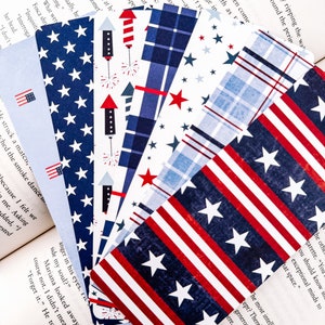 May include: A set of six patriotic bookmarks featuring different designs with red, white, and blue colors. The designs include stars, stripes, and fireworks.