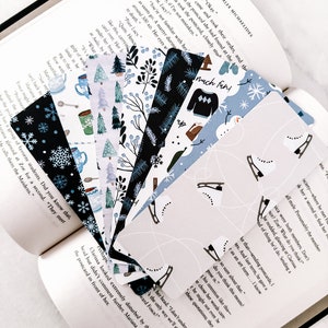 May include: A collection of colorful bookmarks featuring winter-themed designs. The bookmarks include snowflakes, trees, a snowman, a cup of hot chocolate, and a sweater with the text "much fun!" printed on it.