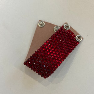Pode incluir: Um bracelete de cristal vermelho com fechos de metal prateado. O bracelete é feito de pequenos cristais redondos que são colocados bem juntos.