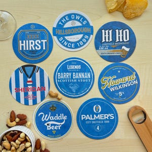 K&ouml;nnte beinhalten: Zehn runde blaue und wei&szlig;e Untersetzer mit verschiedenen Designs und Texten. Die Untersetzer zeigen Namen wie "Hirst", "Sheridan", "Waddle Beer", "Palmer's", "Howard Wilkinson", "Barry Bannan", "The Owls" und "Hi Ho".