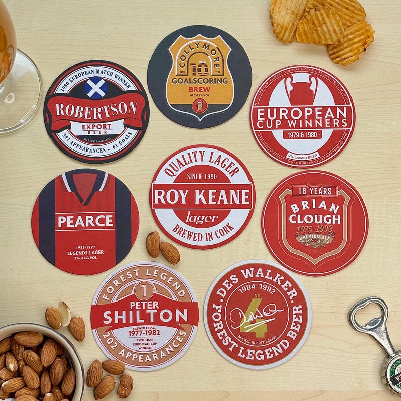 May include: Ten round coasters with red, white, and black designs featuring names and numbers of famous soccer players. The coasters are on a wooden surface with almonds in a bowl.