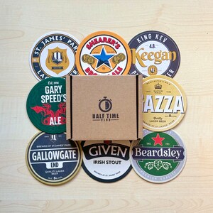 May include: A collection of nine round coasters featuring various brewery logos and names, including "Gary Speed's", "Gallowgate", "Given", "Beardsley", "Shearer's", "King Kev Keegan", "Gazza", and "St. James Park". The coasters are arranged in a circle around a brown box with the words "Half Time Club" printed on it.