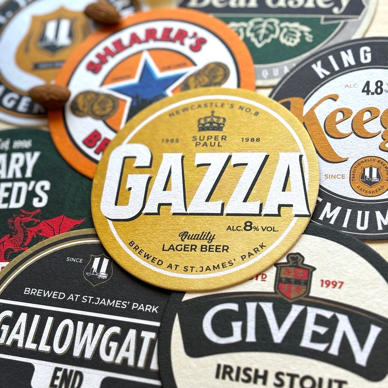 May include: A collection of round, colorful coasters with various brewery logos and names. The coasters are made of cardboard and have a textured surface. The coasters feature the names "Shearer's", "Gazza", "Gallowgate", "Keegan's", and "Given".