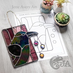 May include: Stained glass crow art piece with iridescent and jewel-toned glass. The crow has a black beak and is hanging from a chain. The artwork is rectangular and features a design of a crow with jewels. The text "Crow with Jewels Piece" is visible.