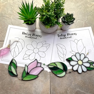 May include: Two stained glass craft kits, one with a daisy design and the other with a tulip design. Each kit includes numbered pieces of stained glass and a pattern sheet.