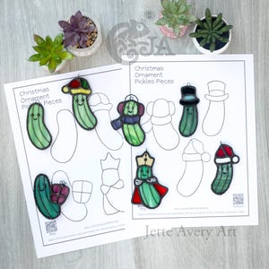 May include: Six stained glass pickle ornaments with various accessories including a Santa hat, top hat, crown, and scarf, arranged on two printed sheets titled Christmas Ornament Pickles Pieces with line art templates and Jette Avery Art text.