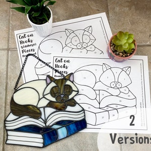 Peut inclure: Deux pages à colorier imprimables en noir et blanc représentant un chat dormant sur une pile de livres. Les pages sont numérotées avec des instructions pour colorier par numéro. Le texte sur les pages indique "Cat on Books (Siamese) Pieces Numbered".