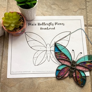 May include: A numbered template for a stained glass butterfly craft project. The template shows a butterfly with 18 numbered sections. A completed stained glass butterfly with pink, blue, and green glass pieces is shown next to the template.