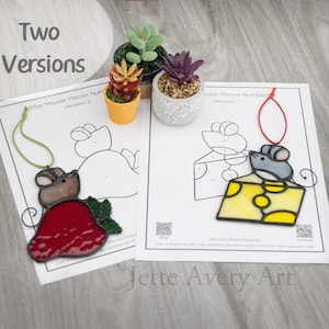 May include: Two stained glass mouse ornaments, one with a red strawberry and the other with a yellow cheese, sit on top of printed patterns. The text "Two Versions" is at the top, and "Jette Avery Art" is at the bottom.