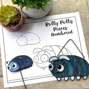 May include: A stained glass Rolly Polly, a type of pill bug, with a blue and white color scheme. The piece is numbered for a stained glass project. The image also includes a printed pattern for the project.