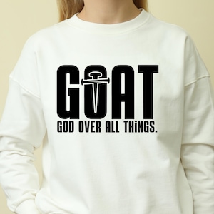 Könnte beinhalten: Weißer Pullover mit schwarzem Text, der "GOAT GOD OVER ALL THINGS." lautet.