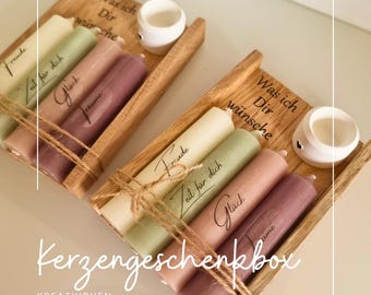 May include: A wooden gift box containing four candles. The candles are tied with twine and feature the words "Freude", "Zeit für dich", "Glück", and "Träume" printed on them. The box also has the inscription "Was ich Dir wünsche". The box is labelled "Kerzengeschenkbox" and "KREATIVCHEN GREVENBROICH".
