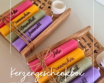 May include: A wooden box containing four candles. The candles are yellow, pink, green, and purple. Each candle has a different message on it: "Liebe", "Donnenschein", "Gesundheit", and "Zuversicht". The box is tied with twine and has a small wooden heart on the side.