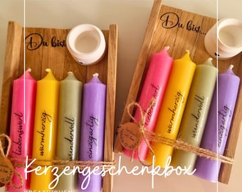 May include: A wooden gift box containing four candles, each a different colour and with a word printed on it. The words are "liebenswert", "warmherzig", "wundervoll", and "einzigartig". The box is labelled "Kerzengeschenkbox" and "KREATIVCHEN GREVENBROICH".