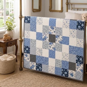 Puede incluir: Una colcha de patchwork que presenta una cuadrícula de cuadrados alternos en varios tonos de azul, blanco y gris. El diseño incorpora patrones florales, colores sólidos y estampados botánicos, cosidos en una disposición cuadrada uniforme.