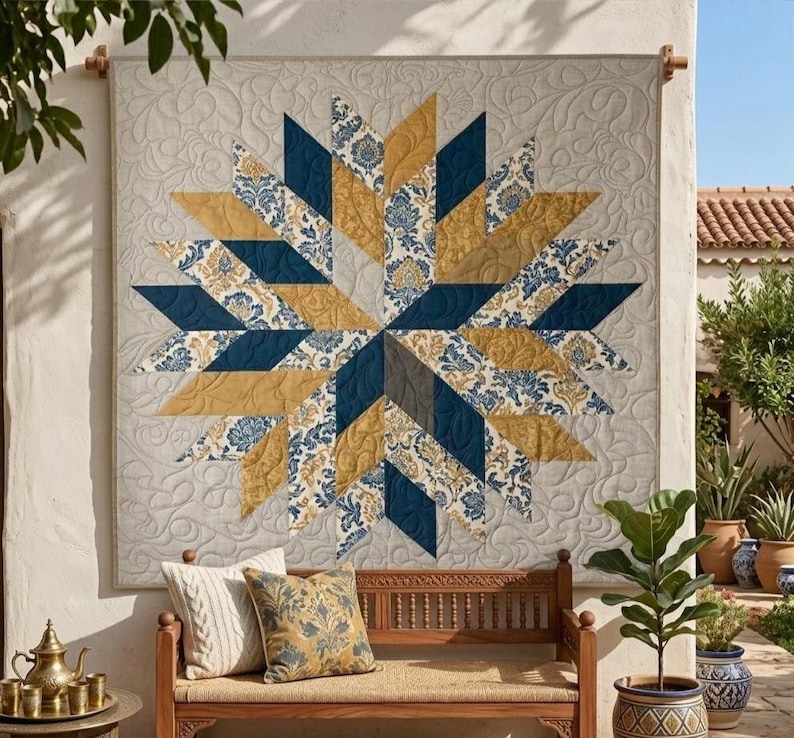 Op de afbeelding: Een grote, decoratieve quilt met een sterrenpatroon. De quilt heeft afwisselende secties van marineblauw, goud en stof met patronen. De achtergrond is lichtbeige met een subtiel bloemenpatroon. De quilt hangt aan een muur.