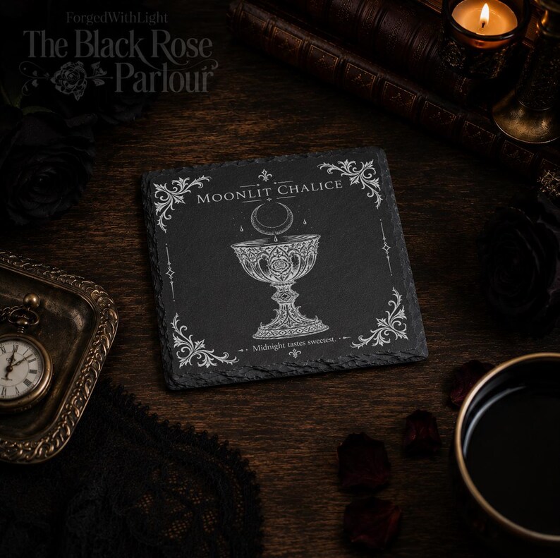 Pu&ograve; includere: Un sottobicchiere quadrato in ardesia nera con un'incisione bianca di un calice sotto una luna crescente. Il testo recita Moonlit Chalice e Midnight tastes sweetest, incorniciato da decorazioni ornamentali agli angoli.