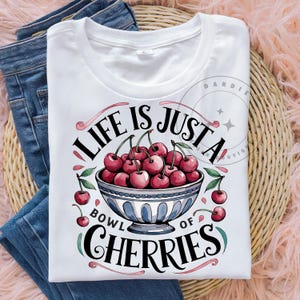 May include: White t-shirt with a graphic design of a bowl of red cherries and the text "Life is just a bowl of cherries".
