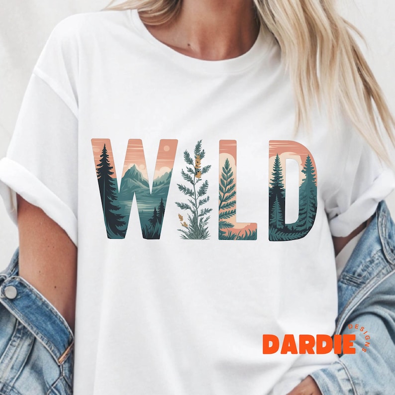 May include: White t-shirt with the word "WILD" in large, colorful letters. The letters are filled with a landscape design featuring mountains, trees, and a sunset. The word "DARDIE" is printed in orange at the bottom right.