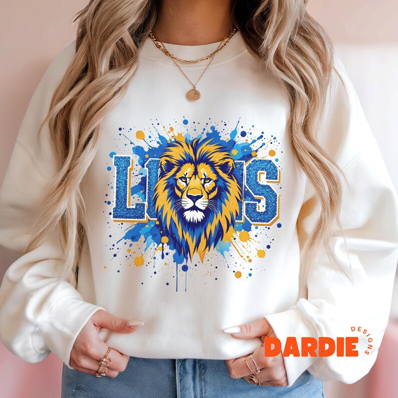 May include: White sweatshirt with a blue and yellow paint splatter design featuring a lion head and the word "LIONS" in blue glitter letters.