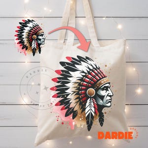 May include: A white tote bag with a colorful illustration of a Native American chief wearing a headdress. The headdress is red, black, and white with gold glitter accents. The background is a pink watercolor wash with gold glitter splatters. The text "DARDIE DESIGNS" is printed in orange on the bag.
