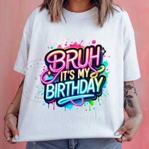 以下が含まれることがあります： 「Bruh it's my birthday」とカラフルなグラフィックがプリントされた白いTシャツです。