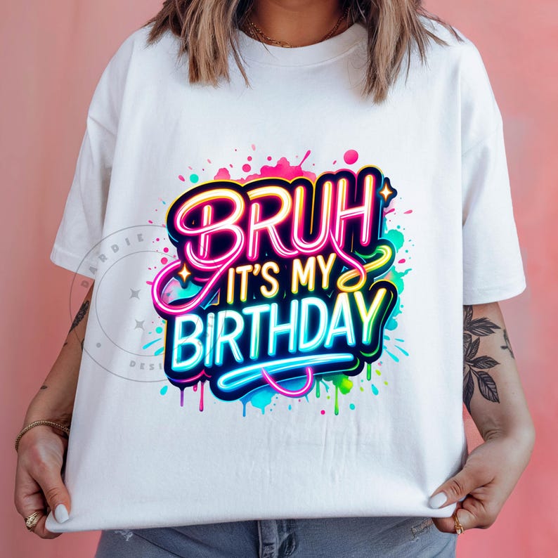 以下が含まれることがあります： 「Bruh it's my birthday」とカラフルなグラフィックがプリントされた白いTシャツです。