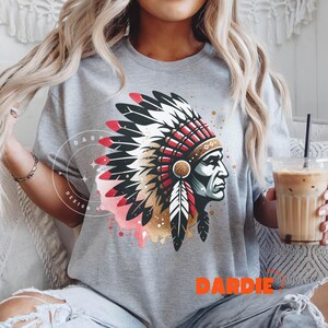 May include: A gray t-shirt with a graphic print of a Native American chief wearing a headdress with red, white, and gold accents. The graphic is surrounded by a pink and gold watercolor effect.
