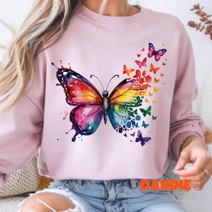 May include: A pink sweatshirt with a colorful butterfly graphic. The butterfly is surrounded by smaller butterflies in various colors. The sweatshirt has the word "DARDIE" printed on the bottom.