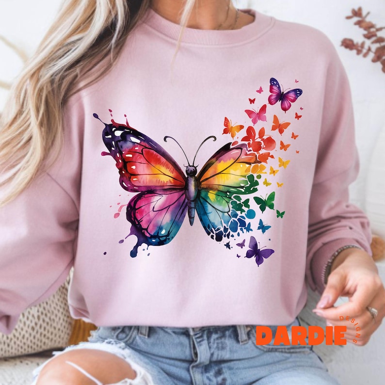 May include: A pink sweatshirt with a colorful butterfly graphic. The butterfly is surrounded by smaller butterflies in various colors. The sweatshirt has the word "DARDIE" printed on the bottom.