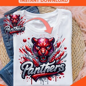 May include: A white t-shirt with a red and silver sequined panther graphic and the word "Panthers" in a glittery font. The graphic is surrounded by red and silver glitter and the word "Panthers" is dripping with silver glitter. The t-shirt is on a wicker basket and a pair of blue jeans.